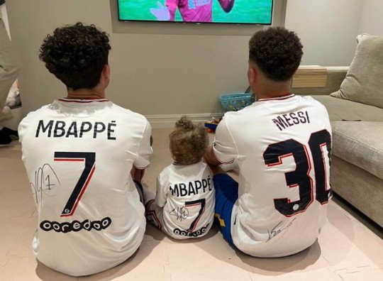 他的孩子们观看比赛直播的背影,他们分别穿着姆巴佩和梅西的签名球衣